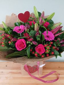 A selection of flowers in rich cerise pink and red, hand-tied in water, wrapped in lovehearts paper and presented in a heart design carry bag. With a red heart pick for added love! Please note roses will be pink in colour.
